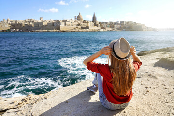 Young traveler woman holds hat looking at Valletta old town travel destination in Malta - obrazy, fototapety, plakaty