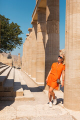 A woman stands in the ancient acropolis of Lindos against the background of the colonade, Greece,...