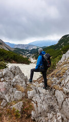 Fototapeta premium Man standing on rock with backpack on scenic hiking trail with view on cloud covered mountain peaks of the Hochschwab Region in Upper Styria, Austria. Snow covered meadows in beautiful Alps in Europe