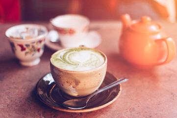 Green Matcha Latte, popular trendy tea with latte art heart shape on top. Served in cafe in ceramic mug on rustic table. Strong shadows and summer sun light