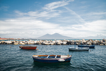 Fototapeta na wymiar Calm blue Tyrrhenian Sea. View from the embankment of Naples to Mount Vesuvius volcano. Pleasure boats moored near the shore and stone breakwaters.