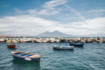 Calm blue Tyrrhenian Sea. View from the embankment of Naples to Mount Vesuvius volcano. Pleasure boats moored near the shore and stone breakwaters.