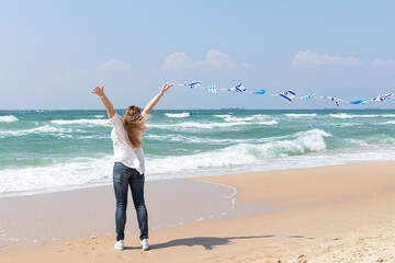 Girl with a garland of Israel flags shows a finger an excellent sign on the seashore. Patriotic holiday Independence day Israel - Yom Ha'atzmaut concept.