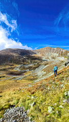 Obraz premium Woman with backpack, view on Haemerkogel in Lower Tauern mountain range, Styria, Austria, Europe. Sunny golden autumn day in Seckau Alps. Scenic hiking trail to Seckauer Zinken on dry, bare terrain
