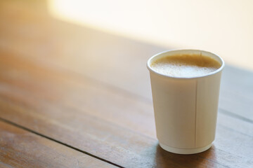 Closeup of disposable takeaway paper cup of hot coffee latte with milk foam on wooden table.