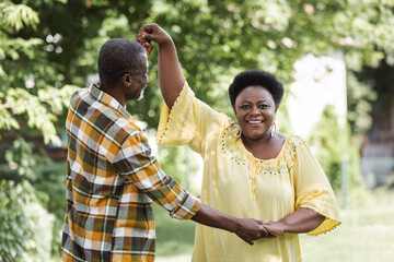 senior african american couple dancing and smiling in park.