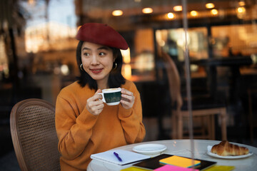 Beautiful Chinese woman drinking coffee in cafe. Young smiling woman enjoy in restaurant