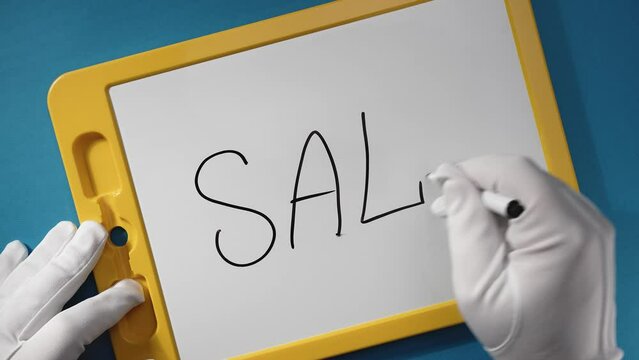 Men's hands in white gloves write the word "SALE" with a black marker on a white plate with a yellow frame.