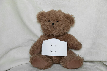 Brown teddy bear and a drawn smiley on paper on a white background, children's toy and joy