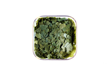 Dry green compound fish feed flakes in a transparent box on White background. Top view