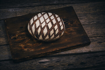 Loaf black rye bread sprinkled with flour on rustic wooden dark background.