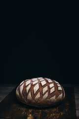 Loaf black rye bread sprinkled with flour on rustic wooden dark background.