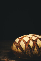 Loaf black rye bread sprinkled with flour on rustic wooden dark background.