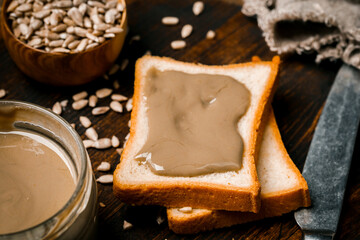 Sunflower paste in a small bowl, a jar and a piece of bread. A modern alternative to nut paste