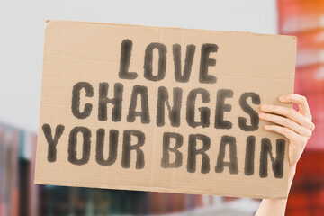 The phrase " Love changes your brain " on a banner in men's hands with blurred background. Awareness. Confusion. Compassion. Disease. Evil. Emotion. Science. Happiness. Set. Blind. Thought. Lover
