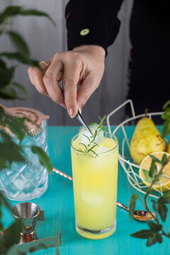 Real woman preparing Pear Collins Cocktail in highball glass or mocktails surrounded by ingredients and bar tools on turquoise table surface