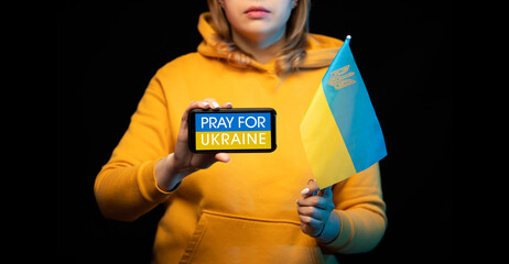 Beautiful Ukrainian girl with a state flag and smartphone in hands with a call PRAY FOR UKRAINE. The actual concept of anti-war support. Russian-Ukrainian war. STOP WAR