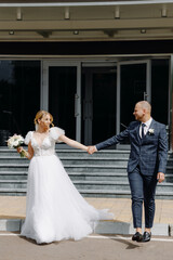Naklejka na ściany i meble Happy bride and groom walking on the background of the hotel entrance