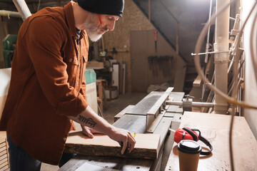 side view of carpenter in beanie measuring board near coffee to go.