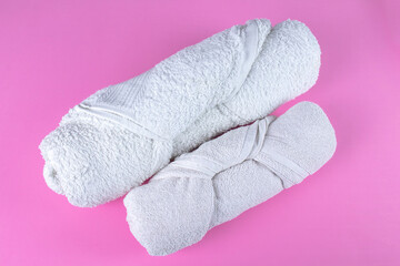 Two folded rolled white bathroom towels on pink background.