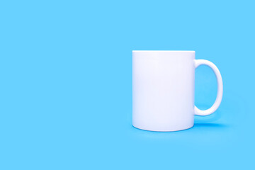 Obraz premium White mug on a blue background with free space for text. White cup with a drink on an empty blue background. Cafe or snack concept. White mug with the possibility of applying advertising or logo