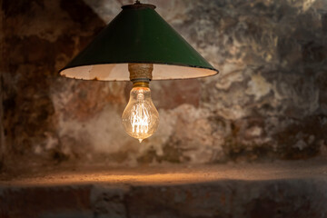 An antique incandescent lamp with a red-hot filament of an elegant shape shines against the background of a brick wall