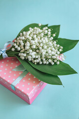 Bouquet of Lily of the valley flowers and gift on blue background.