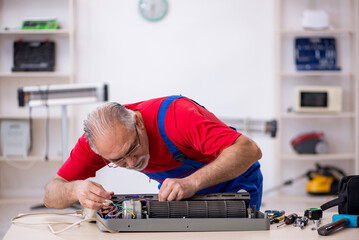 Old repairman repairing air-conditioner at workshop