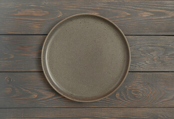 Empty rustic dark plate on a gray wooden background. Top view, with copy space.