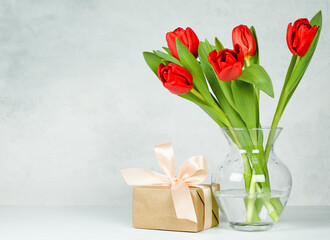 vase with red tulips and gift box on light concrete background