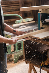 cropped view of tattooed carpenter working on bench thicknesser in workshop.
