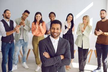 Portrait of successful young african american businessman who is looking at camera with confident expression. Man stands with folded arms against background of applauding people. Business concept.