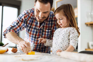 Cute small girl baking a cake with her father in the kitchen