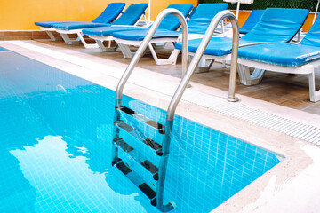 Swimming pool with stair. Grab bars ladder in the blue swimming pool