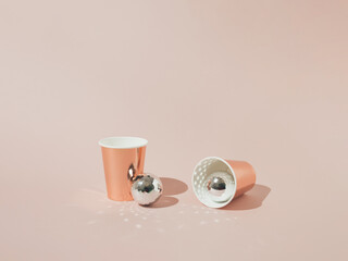 Two rose gold paper beverage cups with shiny disco balls on rose background. Minimal concept.