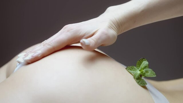 The hand smears the cream on the buttocks. ACTION. Massage of the buttocks and smearing with white cream. The buttocks are prepared for wrapping and massage. Fallen mint leaf