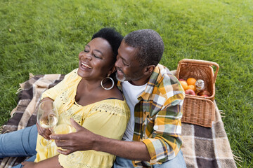 high angle view of joyful and senior african american couple clinking glasses of wine during picnic in park.