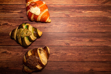 Croissants with different flavors on a dark wooden table. Free space for text. Top view.