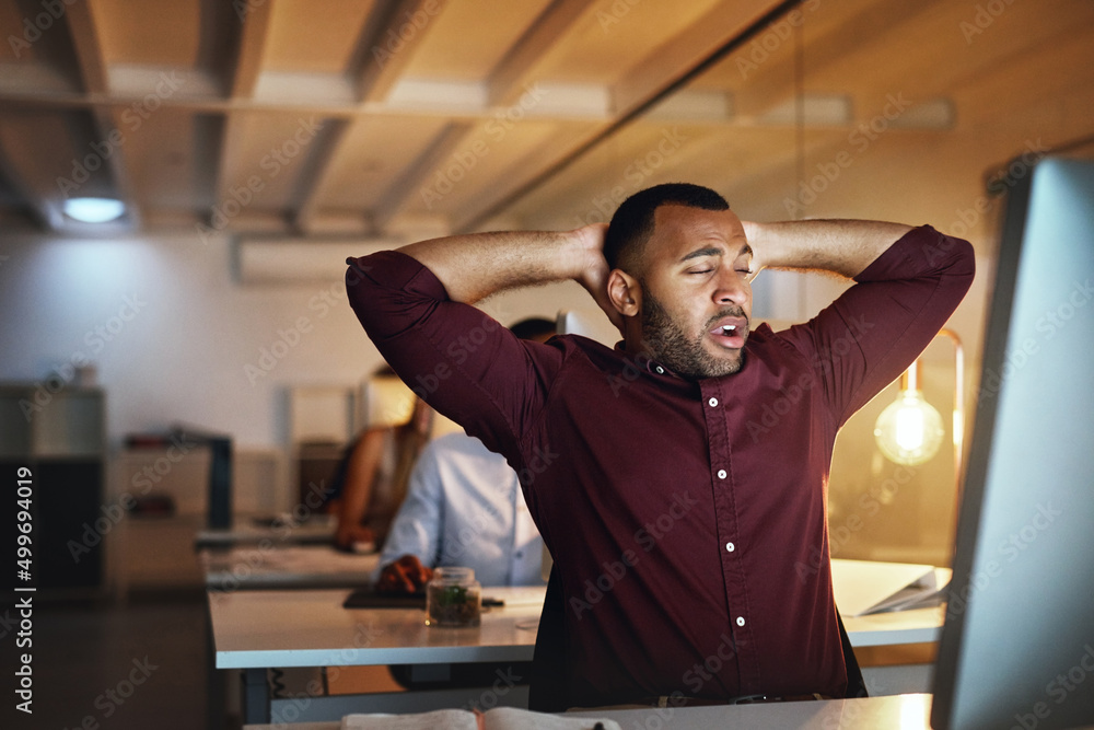 Poster must... stay... awake.... shot of a young businessman looking exhausted while working late in an off