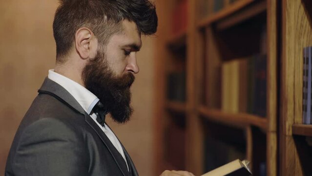 Mature man in library and enjoys reading. Bearded man in suit looks satisfied. Relax pleasure and leisure, hobby concept. Man picking a book in a library.
