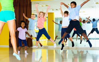 Group of friendly smiling positive tweens jumping with female coach during exercising in choreography class