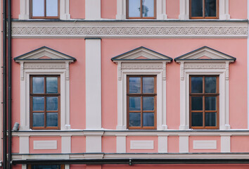 Obraz premium Windows on the facade of a pink house in the central historical part of the city. Beautiful decorative architecture with reliefs on white cornices and pilasters in Lviv, Ukraine.