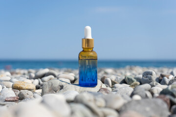 A dropper bottle of face serum or natural oil standing on the stones on the beach