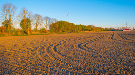 Plowed field with furrows in sunlight at sunrise below a blue sky in spring, Almere, Flevoland, The...