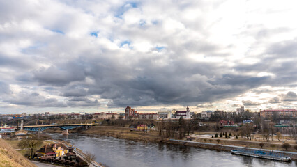 The movement of gray rain clouds over the river and a panorama of the city. View of the embankment along the river and the road bridge.