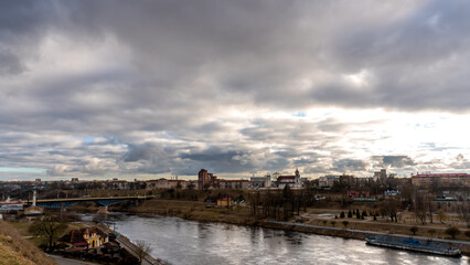 Fototapeta na wymiar The movement of gray rain clouds over the river and a panorama of the city. View of the embankment along the river and the road bridge.