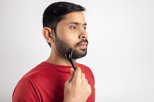 Indian guy in white background using microneedling for beard growth.