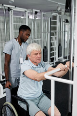 Fototapeta na wymiar Portrait of senior man using wheelchair in gym and doing rehabilitation exercises