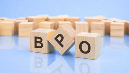 three wooden cubes with the letters BPO on the bright surface of a pale lilac table. the inscription on the cubes is reflected from the surface of the table. business concept