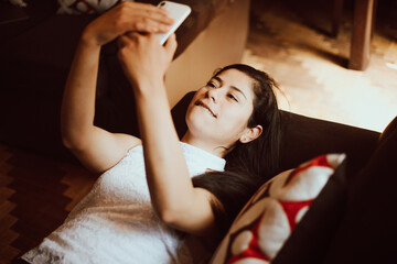 Mujer contenta usando su teléfono móvil mientras descansa en el sillón de casa. Concepto de tecnología y personas.